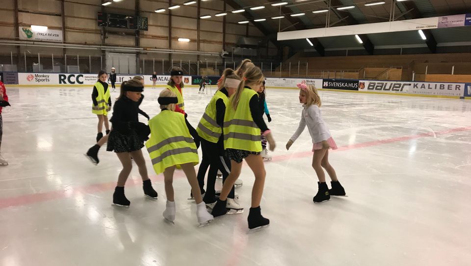 Konståkningsgrupp med barn tränar på isen iklädda reflexvästar
